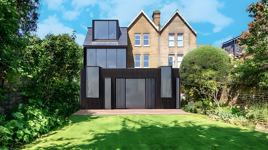 Modern double-storey rear house extension with a sleek black design, featuring large glass windows and a roof skylight, integrated with a traditional Victorian brick house set in a lush garden with mature trees.