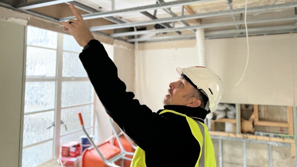 A construction worker in a high-visibility vest and helmet inspecting the framework of a Georgian house extension under construction.