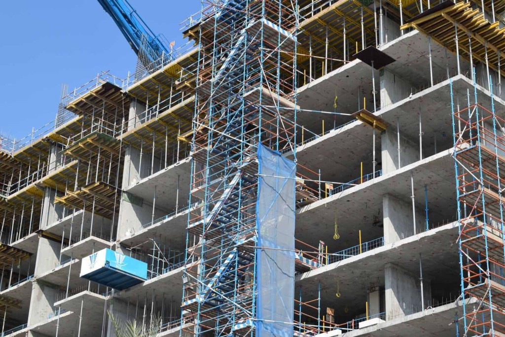 Close-up view of a multi-story building under construction, featuring extensive scaffolding and concrete slabs. This image illustrates the process of adding residential apartments above existing commercial spaces, enabled by the government's update on prior approval rights for upward extensions without needing traditional planning permission.