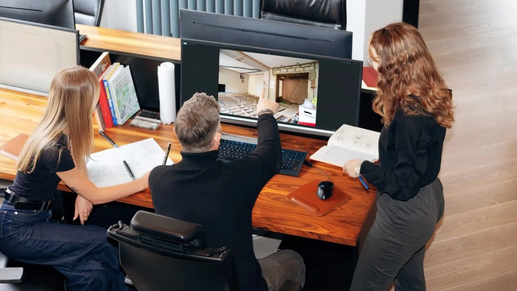 Architectural team reviewing a building renovation project on a large monitor, analysing site photographs, floor plans and structural changes to assess the strength of a fallback position in a planning permission application.