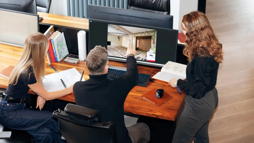 Architectural team reviewing a building renovation project on a large monitor, analysing site photographs, floor plans and structural changes to assess the strength of a fallback position in a planning permission application.
