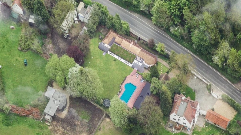 Aerial view of a residential property and surrounding land showing an existing dwelling, outbuildings, swimming pool and extensive garden plot, illustrating site evidence and lawful fallback development potential for a planning permission application.