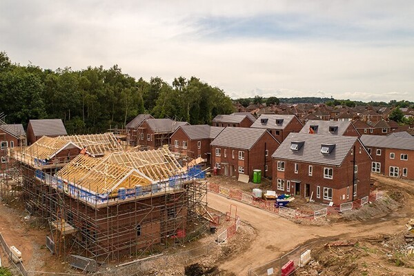 A housing development site with several newly built brick homes in the final stages of construction, surrounded by scaffolding and construction materials. The image highlights the issue of councils failing to meet their Five-Year Housing Land Supply (5YHLS) targets, leading to increased opportunities for developers to build in areas like the Green Belt. 