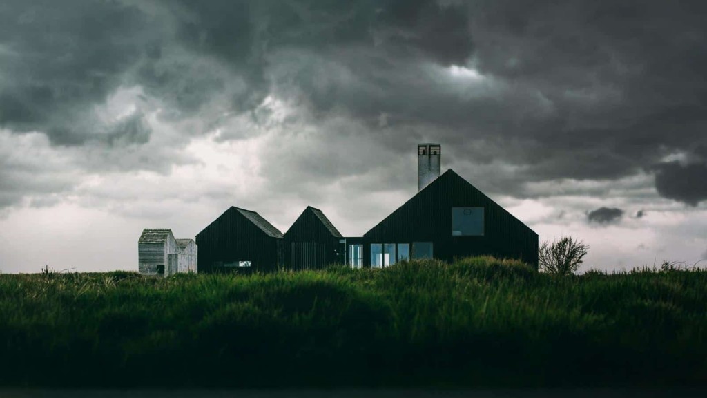 Modern development on agricultural land of a residential dwelling spread and interlocked barn shaped units showcasing the natural barn materials as well as the modern with glass units that brightly light the residence during the twilight hour and incoming storm
