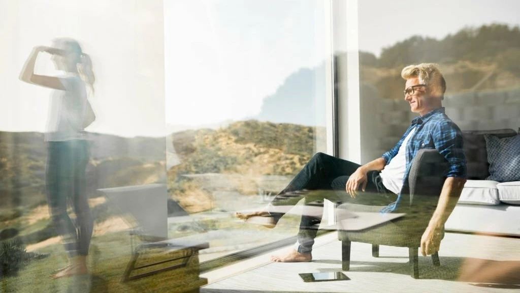 Two people relaxing in a modern home with large windows overlooking a natural landscape, reflecting on the potential for nearby golf courses in green belt areas to be considered for development.