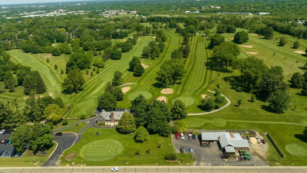 Aerial view of a golf course within a green belt area, showcasing expansive green spaces and nearby urban development, highlighting potential areas impacted by green belt reform.