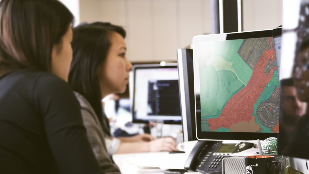 Two urban planners working on a computer with a digital map on the screen, showing land classification areas marked in red and green, likely related to Green Belt assessments. This image represents the process of evaluating land for development based on Green Belt purposes, such as urban containment and environmental protection. It highlights the use of Geographic Information Systems (GIS) in assessing land suitability for housing, infrastructure, and preserving natural landscapes. This is essential for understanding how councils assess Green Belt purposes and make land release decisions.