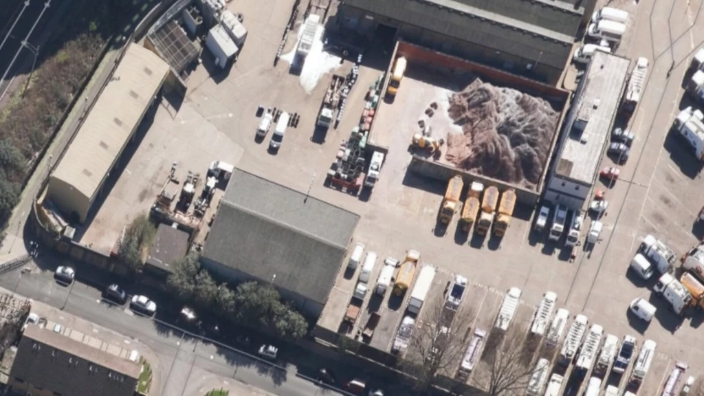Aerial view of industrial recycling centre in Tottenham Green Belt with piles of materials, heavy machinery, and commercial vehicles.