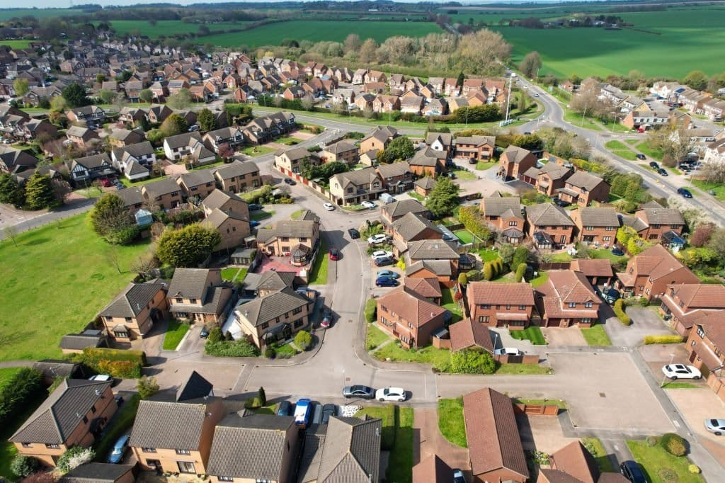 Overhead shot of a new residential housing estate with brick-built detached homes, cul-de-sacs, and landscaped gardens, showcasing sustainable suburban development in the green belt.