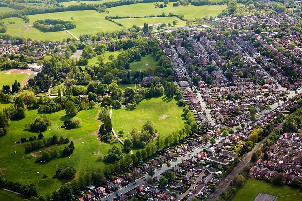 Aerial view of a suburban area with dense housing adjacent to spacious green parks, illustrating the integration of residential development with green spaces in a suburban setting.