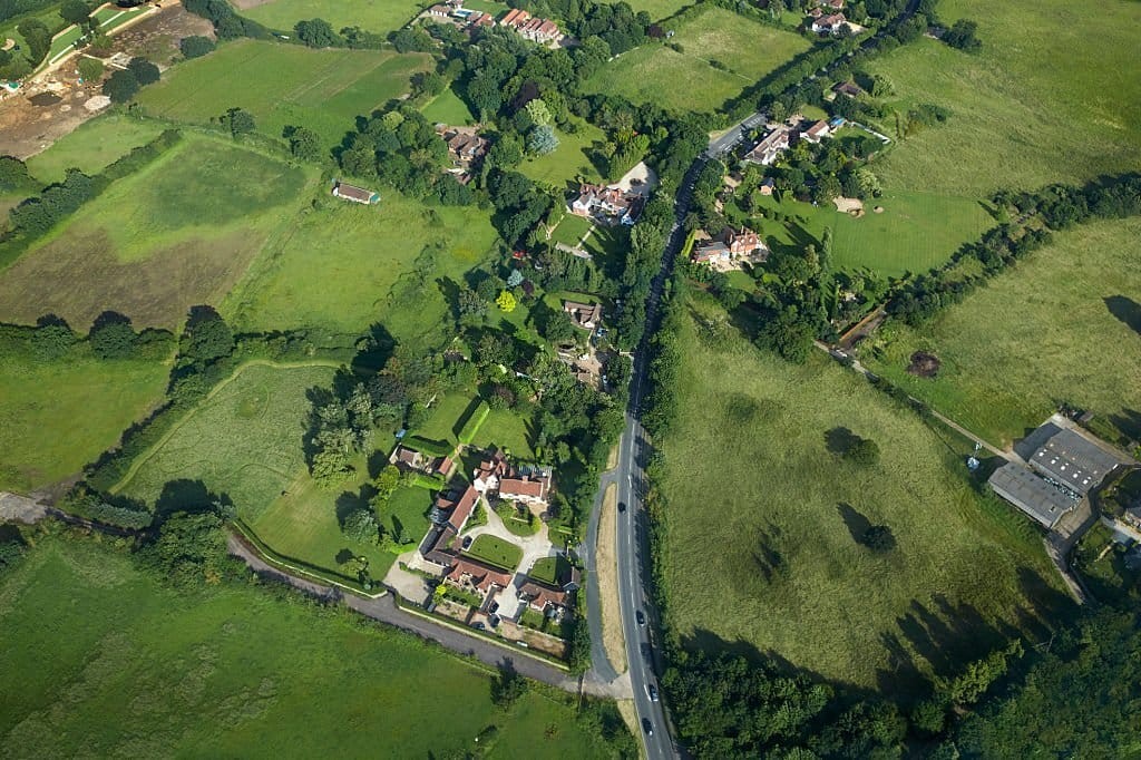 Aerial photograph of green belt land showing a mix of agricultural fields, residential properties, and winding roads, highlighting the balance of development and rural charm in addressing housing shortages.