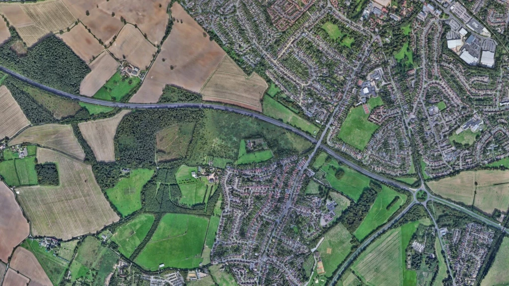 Aerial satellite view of farmland and housing estates on the urban edge, showing how Green Belt planning uplift can drive land value increases.