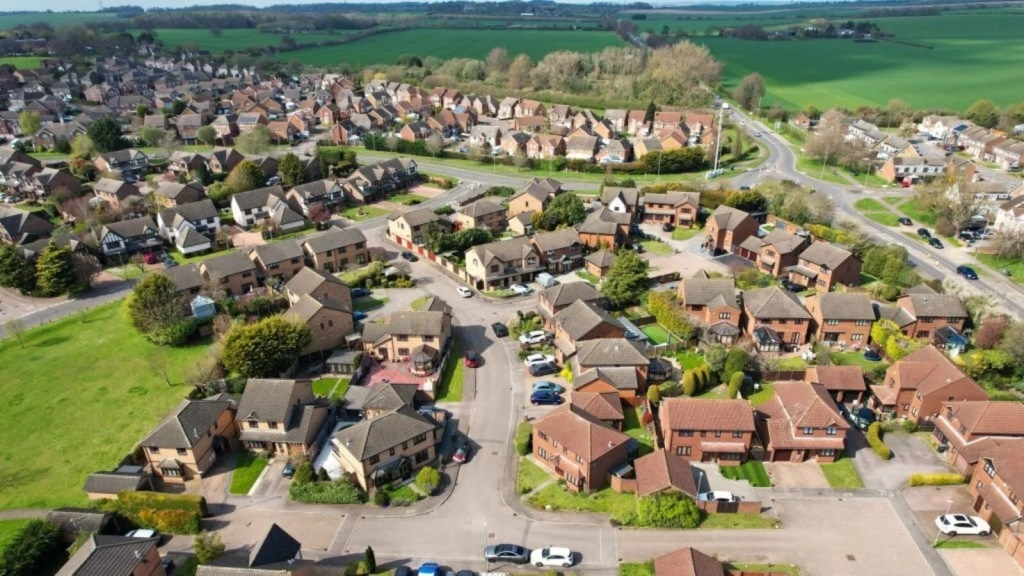 Aerial view of suburban houses bordering open countryside, illustrating the Green Belt planning uplift and the resulting land value increase.