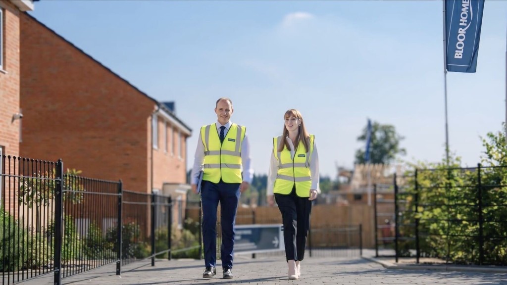 Angela Rayner, Deputy Prime Minister and Secretary of State for Housing, Communities and Local Government, wearing a high-visibility vest while walking through a newly built housing development alongside a colleague. They are inspecting the progress of the construction, which appears to be taking place on previously protected land. The image reflects the practical aspects of urban development, especially in the context of Green Belt land discussions, planning permissions, and housing projects in the UK.