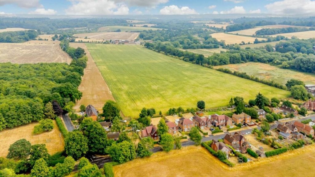 Aerial view of a countryside area showing a clear boundary between developed land with houses and expansive green fields, representing the key purposes of the Green Belt in urban planning. The image illustrates the importance of the Green Belt in preventing urban sprawl, maintaining the separation between towns, and safeguarding the countryside from encroachment. This visual is pertinent to discussions on the designated roles and purposes of Green Belt land in preserving rural landscapes and controlling urban expansion.