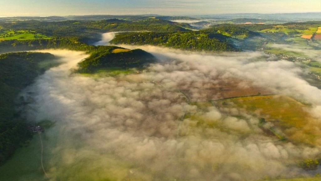 Aerial view of a lush, rolling landscape covered in morning mist, with patches of forest and open fields visible, emphasising the natural beauty and ecological importance of Green Belt areas.