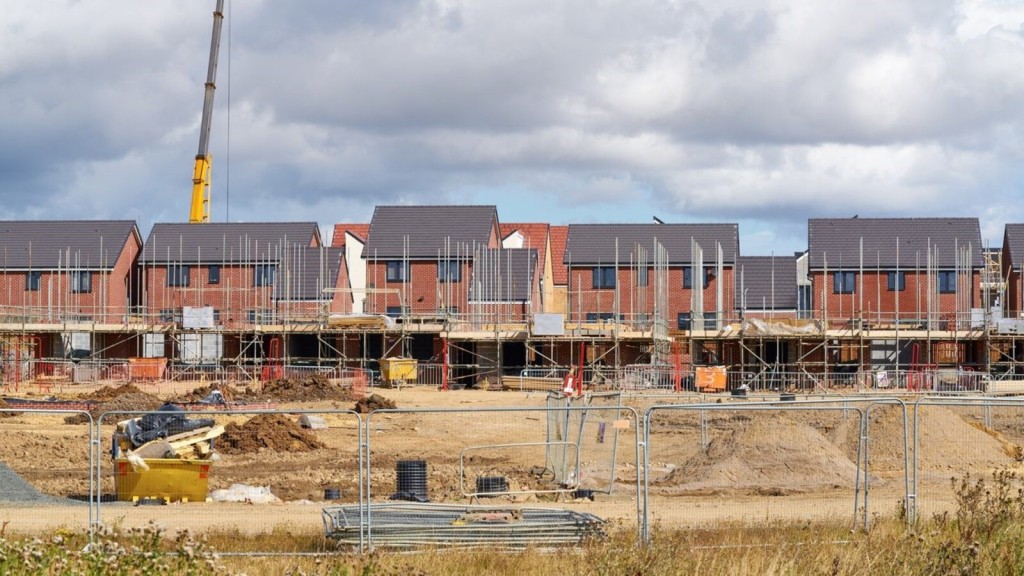 Rows of partially constructed red-brick houses with scaffolding and construction equipment, illustrating the reduction of Green Belt openness.