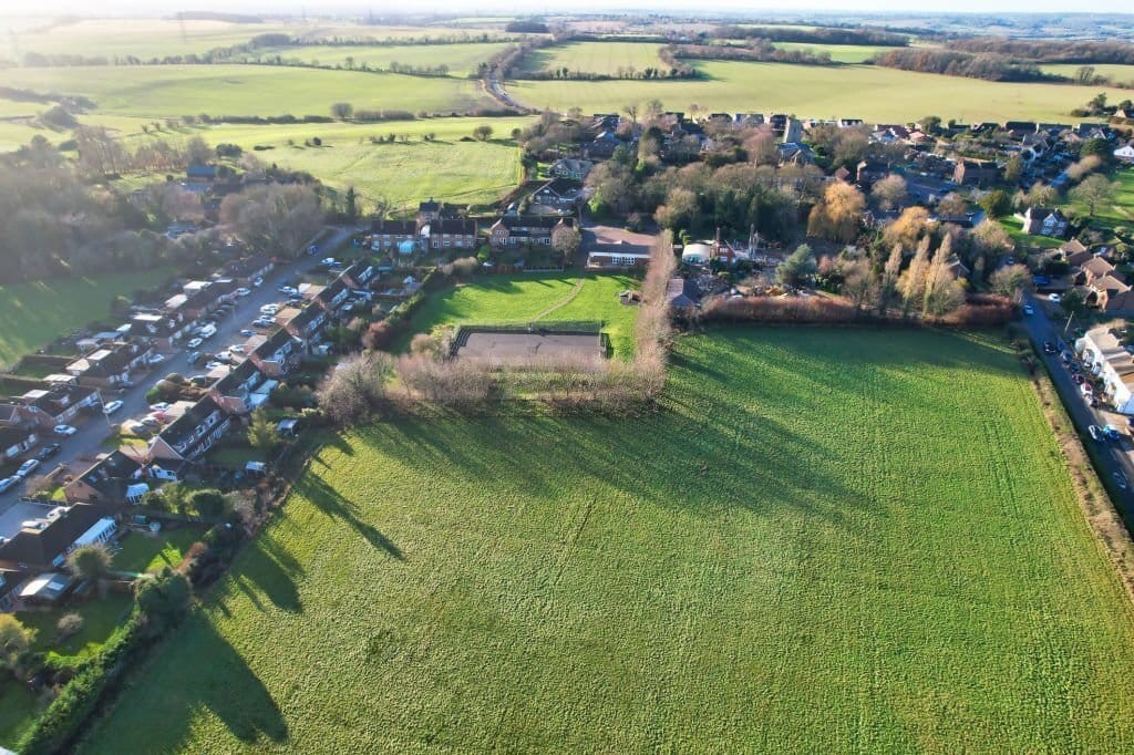 Aerial view of a serene suburban neighborhood adjacent to vast green fields, illustrating the interface of urban and rural landscapes.