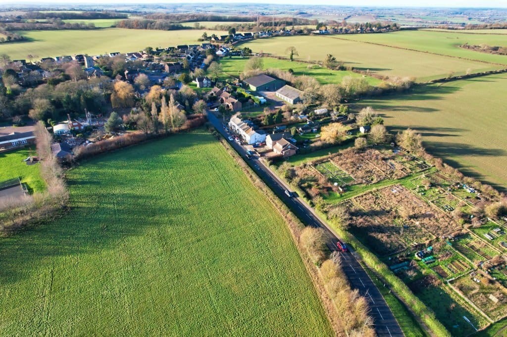 Aerial view of a lush greenbelt land in the countryside with a small village, agricultural fields, and allotment gardens, illustrating rural land use and community planning.