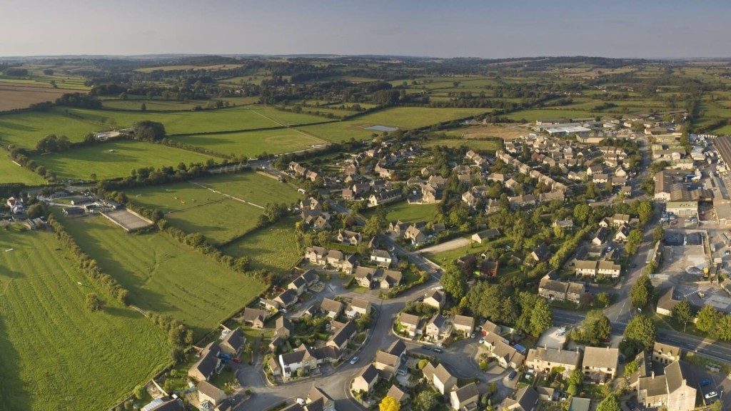 Aerial view of an English village surrounded by expansive green fields, illustrating the concept of Green Belt land in the UK. This image captures the contrast between rural landscapes and urban development, highlighting the importance of Green Belt planning policies aimed at preventing urban sprawl and preserving countryside openness.