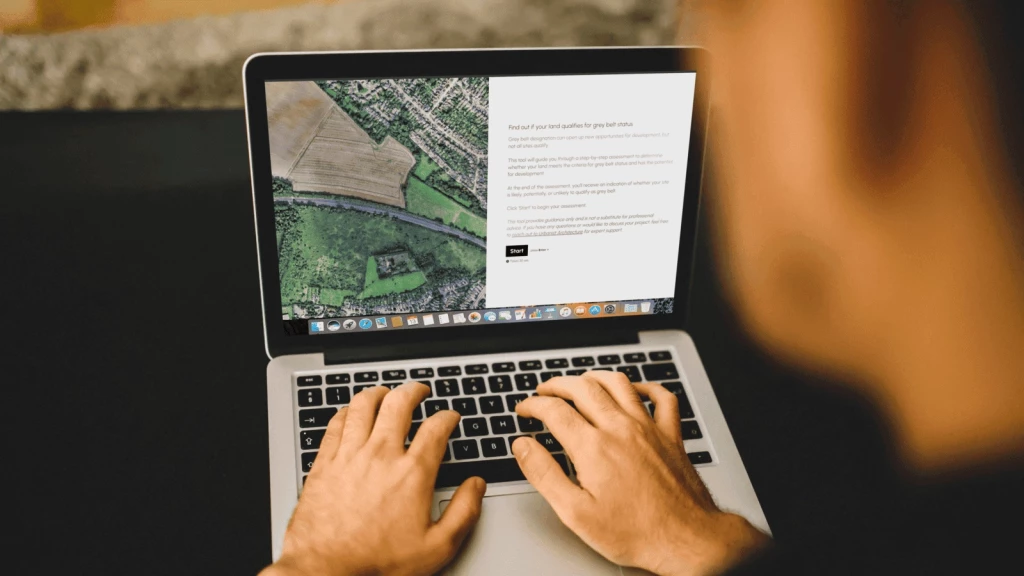 A property developer using the Grey Belt Assessment Tool on a laptop, reviewing an aerial map of a site alongside a step-by-step assessment to determine its eligibility for grey belt status. The tool provides guidance on planning potential and next steps for development.