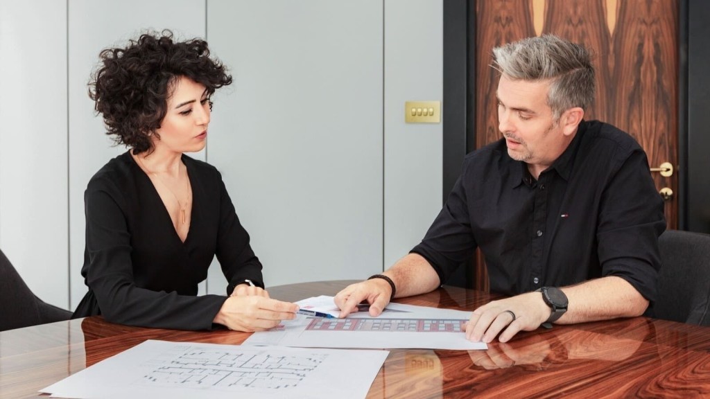 Two architects reviewing blueprints at a table, discussing plans for sustainable development within the Green Belt. The image captures a professional consultation, reflecting Urbanist Architecture's expertise in navigating grey belt policies to create eco-friendly housing solutions. This highlights the firm's commitment to addressing the UK's housing crisis through strategic and environmentally conscious planning.