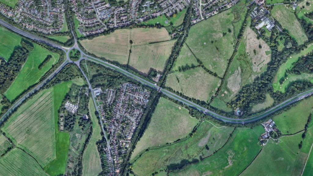 A satellite image showing developed and undeveloped land, roads and natural boundaries, illustrating how physical features can inform Grey Belt assessment against Green Belt purposes (a), (b) and (d): checking unrestricted sprawl, preventing neighbouring towns from merging, and preserving the setting and special character of historic towns.