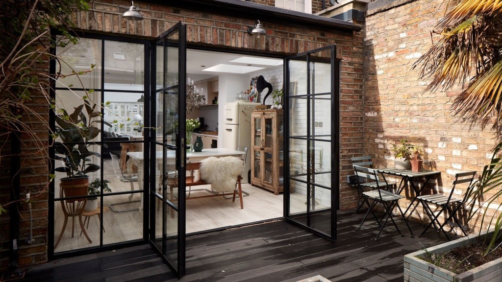 A modern house extension with seamless interior design, featuring crittall-style glass doors opening to a cozy patio, blending rustic brick walls with elegant interior architecture for functional living