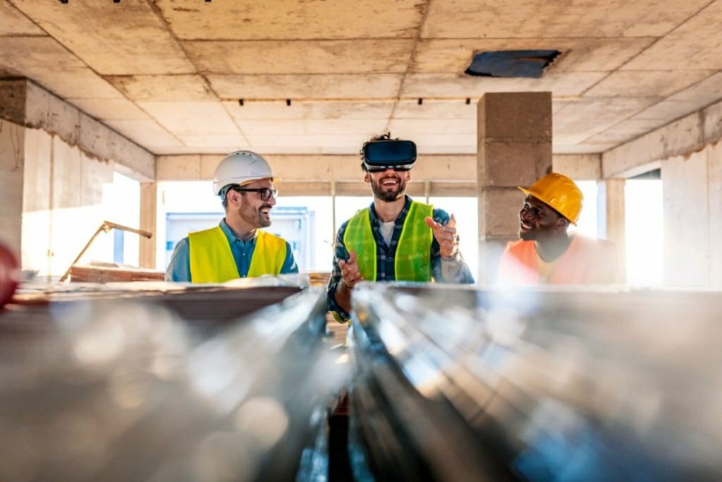 Three construction professionals with safety helmets inside a building under construction, one wearing a VR headset, showcasing modern technology integration in construction management and teamwork.