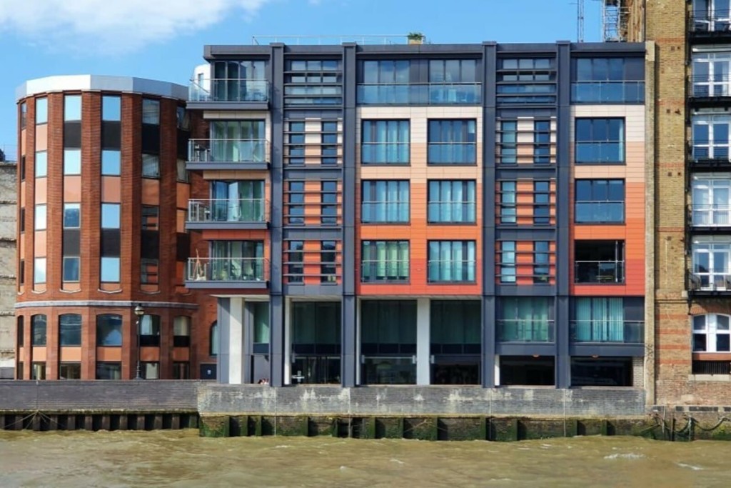 Modern riverfront apartment buildings with a combination of red brick and dark panel facades, featuring large windows and balconies, exemplifying contemporary urban residential architecture.