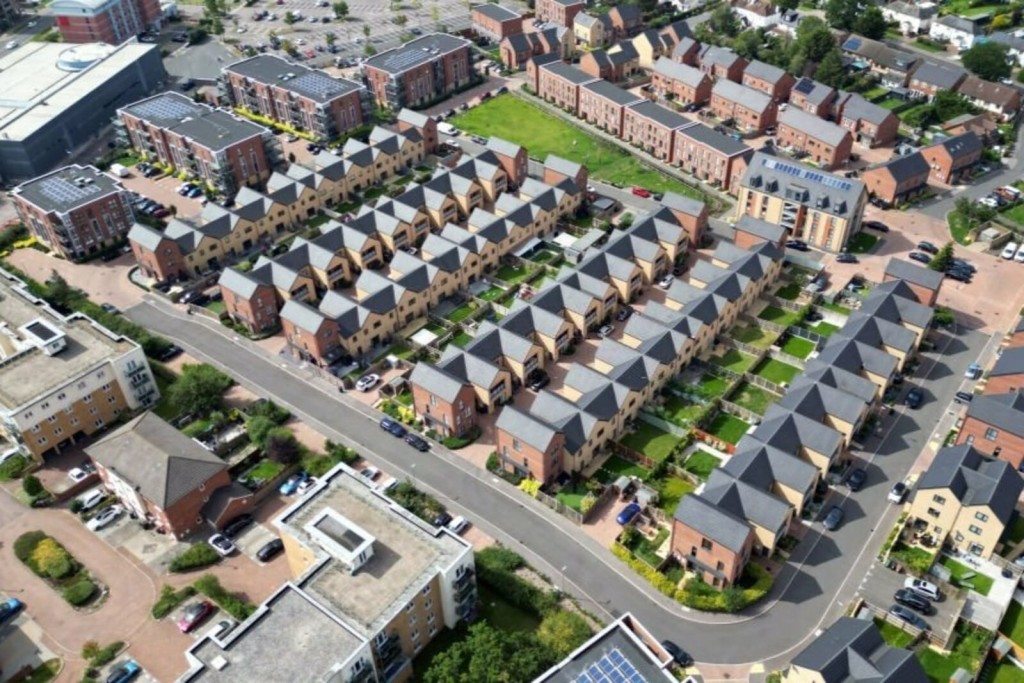 Aerial view of a well-planned residential housing estate with a variety of brick townhouses and landscaped gardens, showcasing organized urban development in a suburban setting.