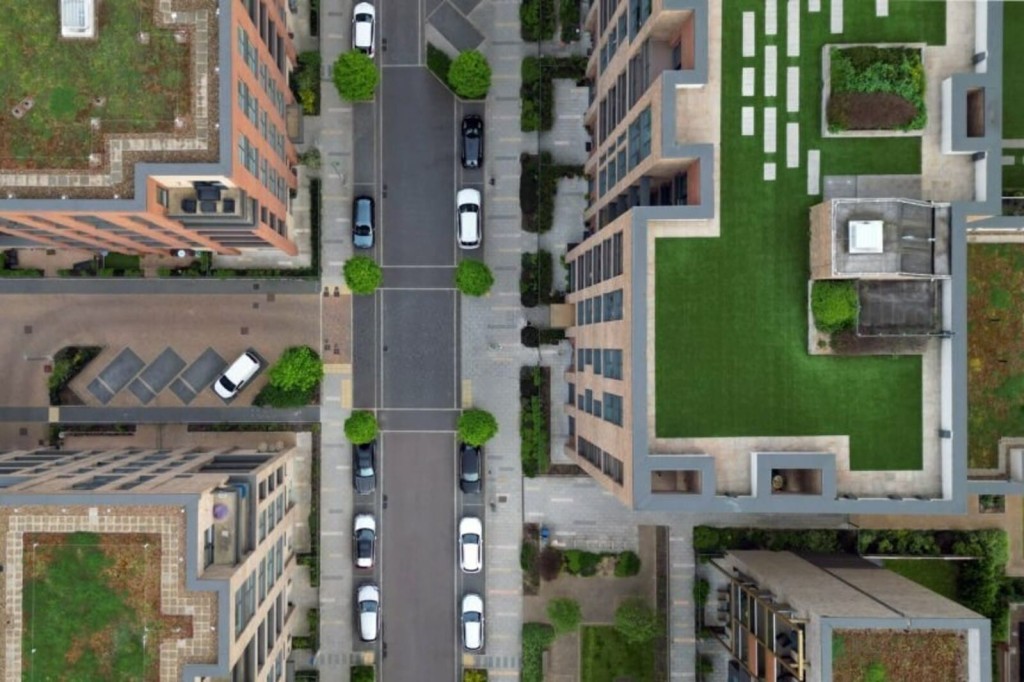 Aerial view of urban residential area showing a well-planned street with parked cars, modern apartment buildings, and neatly landscaped green spaces, illustrating efficient urban design and development.