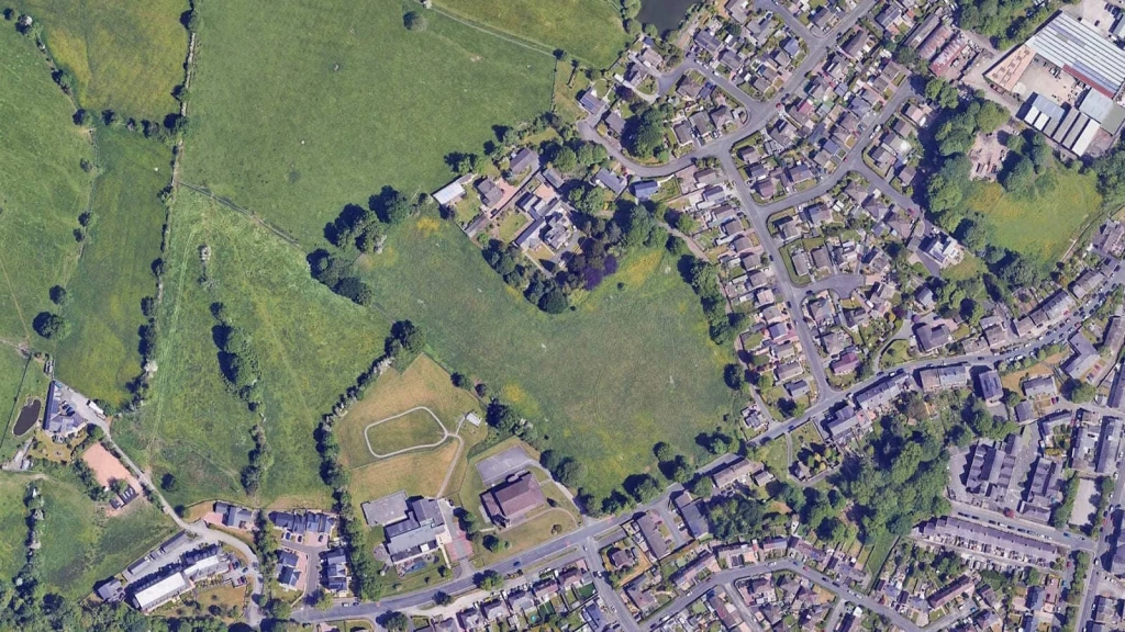 Aerial view of an open greenfield site surrounded by houses, roads and community buildings, representing potential Grey Belt land for new homes.