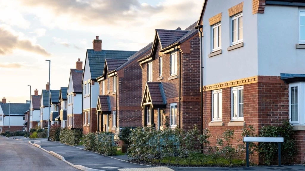 Row of modern brick and render suburban houses with driveways on a quiet street, typical UK new-build estate linked to rising rents and house prices.