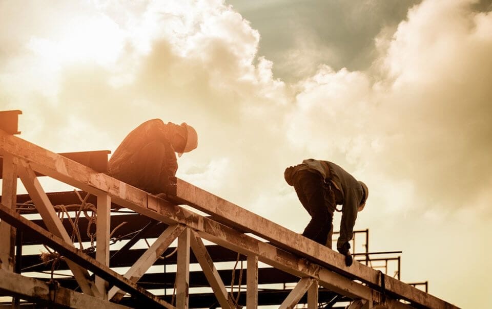 Construction workers in safety helmets working on the framework of a building against a dramatic cloudy sky, symbolising industrial progress and architectural planning.