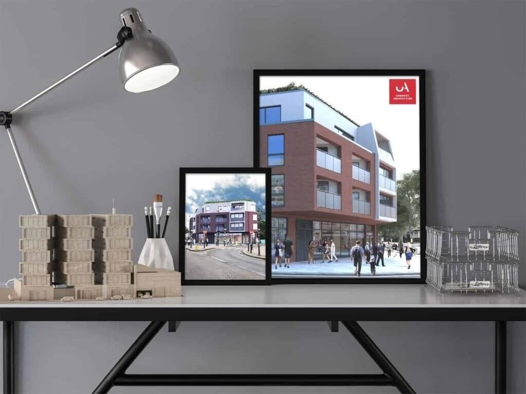 Architect's modern workspace featuring a sleek black desk with architectural models and drawing tools, illuminated by a silver adjustable desk lamp. Two framed architectural renderings of a contemporary urban building project are displayed, branded with the Urbanist Architecture logo.