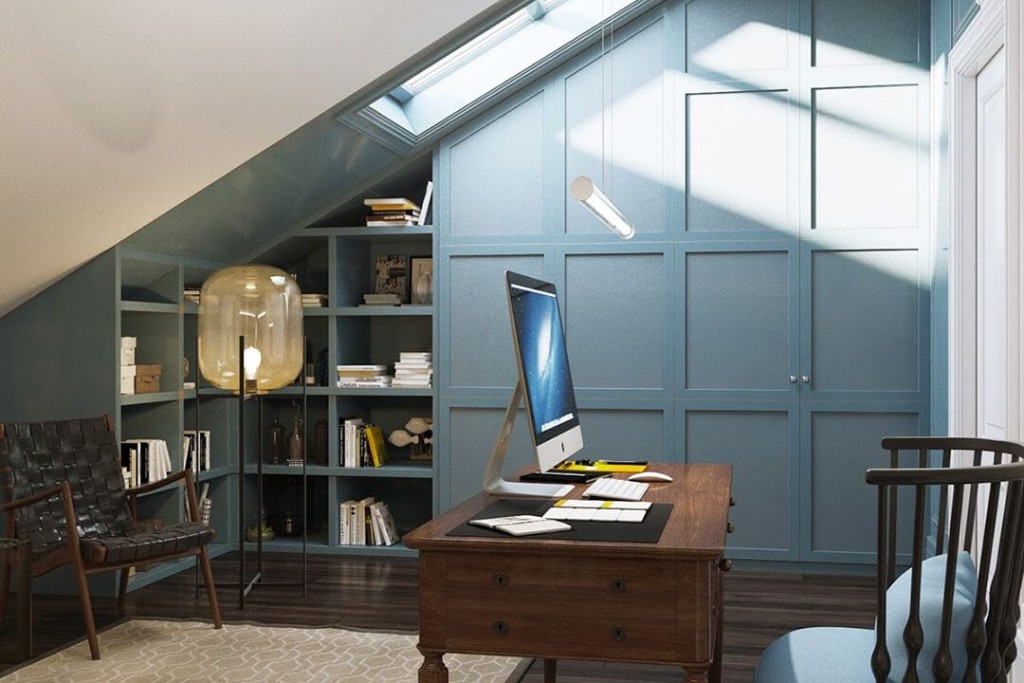 Chic attic home office in London featuring a sloped ceiling with a skylight, a stately wooden desk with an iMac, surrounded by built-in blue bookshelves and elegant furniture, creating a cosy yet sophisticated workspace.