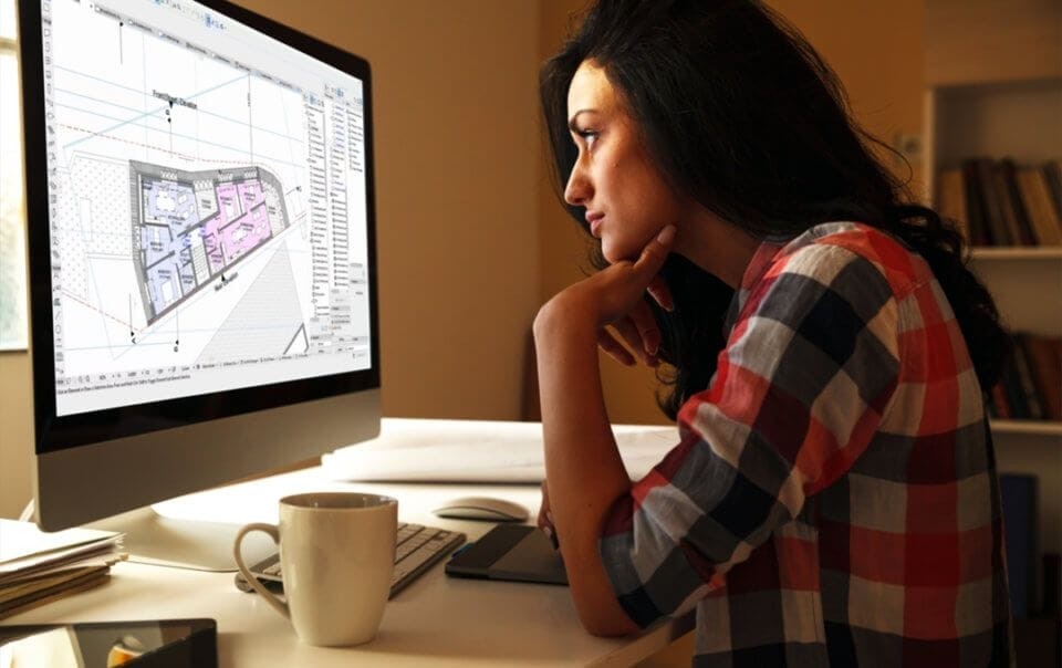 Focused female architect reviewing a 3D building plan on a computer screen in a warmly lit home office, with a coffee mug and design tools on the desk, embodying professional home workspace concept in London, UK.