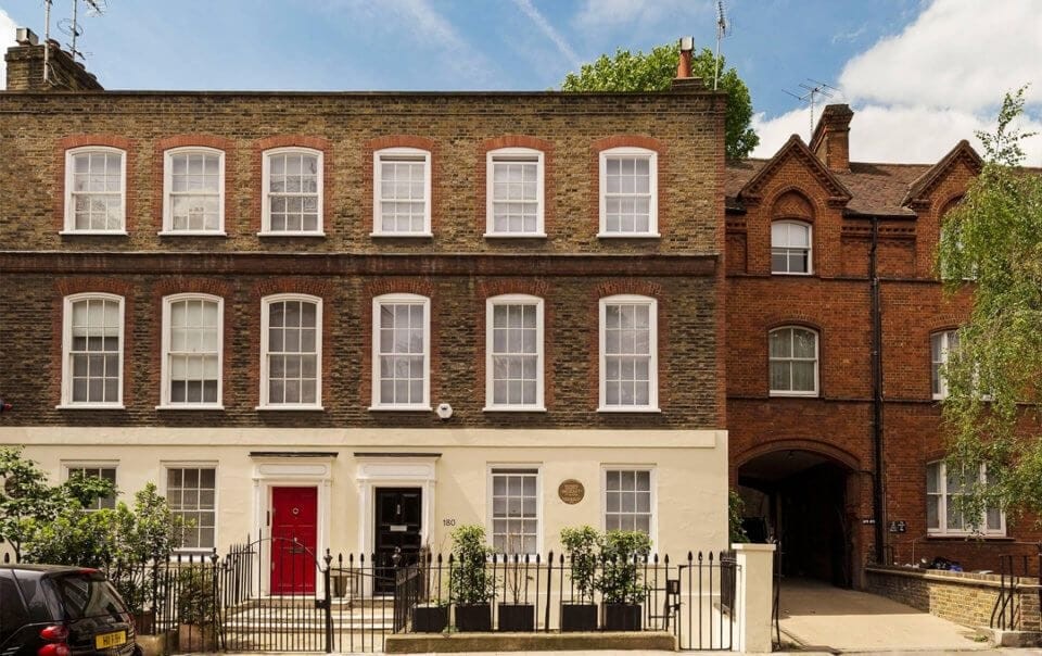 Beautiful listed townhouse converted into fully residential family homes in London with ornate black fence, white brickwork on the ground floor and traditional brown and red brick on the second and third floor with the neighbouring propoerty having a set back arched entrance with deep red brick colouring