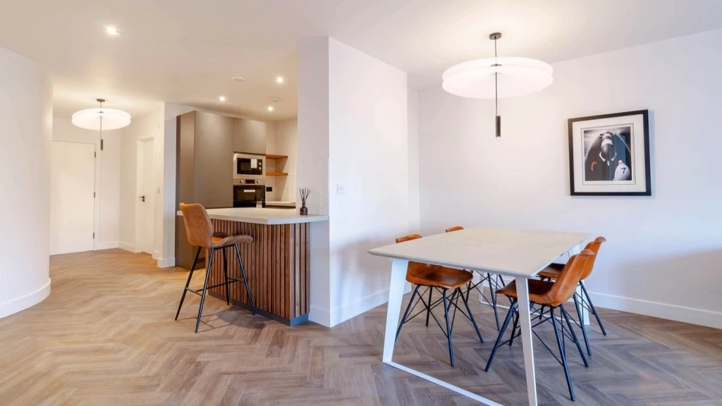 Modern open-plan kitchen and dining area with sleek gray cabinets, white subway tile backsplash, and herringbone-patterned flooring, illuminated by natural light and a stylish overhead pendant lamp.