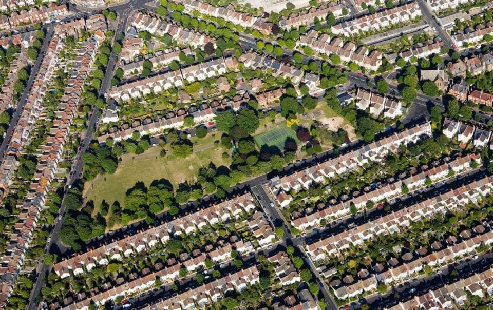 Aerial view of a conservation area in London, UK, featuring rows of terraced houses with uniform gardens, punctuated by a lush green public park, highlighting the organised urban planning and green spaces in residential neighborhoods.
