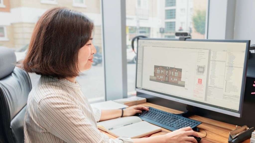 A professional architectural designer woman working on a CAD architectural design on a computer in a bright office setting, with a focus on eco-friendly building concepts.