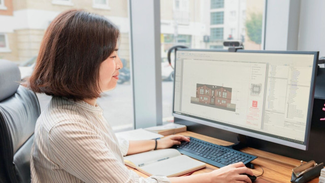 Image cover for the article: Two architects reviewing blueprints and architectural plans at a conference table in a well-lit office, with a laptop and coffee mug in view.