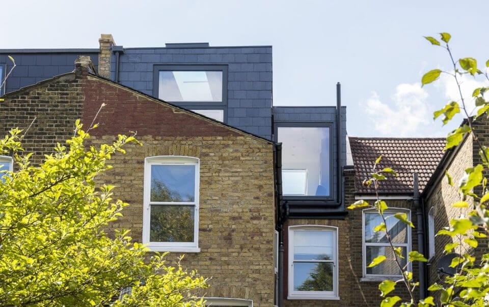 An L-shaped dormer loft conversion on a Victorian terraced house, showcasing modern windows and slate roof against the traditional brickwork, exemplifying a seamless blend of contemporary design with classic architecture in an urban setting.