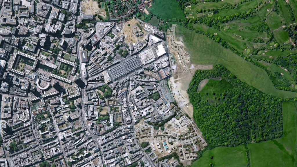 Satellite view showing the edge of dense urban development meeting green space, illustrating the challenge of infrastructure integration one year on with Labour in charge and the rollout of Grey Belt housing reforms.