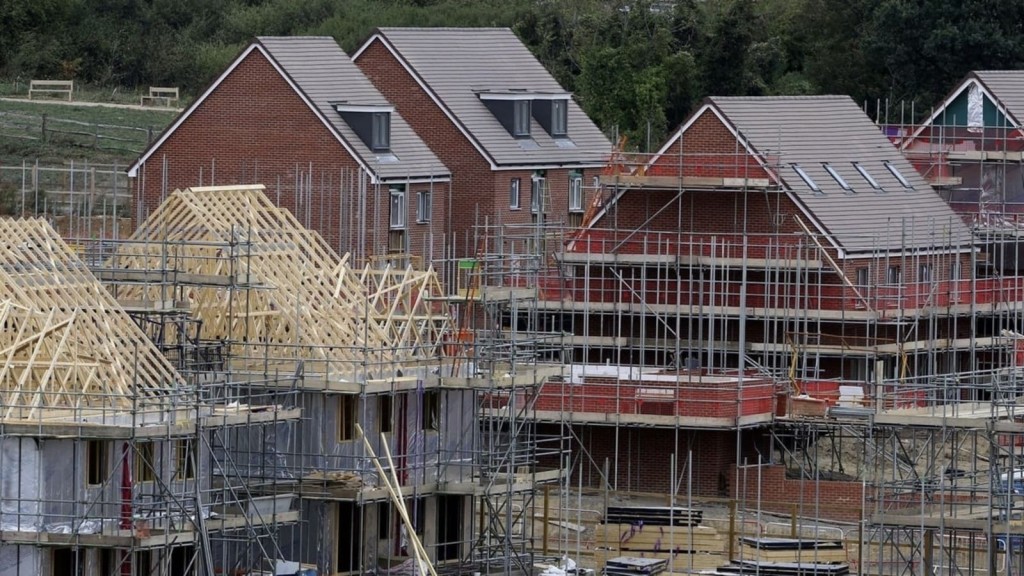 New homes under construction with scaffolding and roof frames, highlighting housing development projects in the UK.