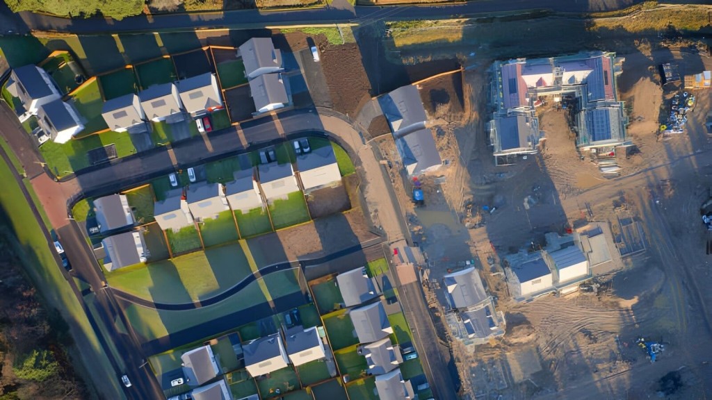 Aerial view of a housing development showcasing new construction on the right side and established homes with manicured green lawns on the left side, illustrating urban planning and residential growth.