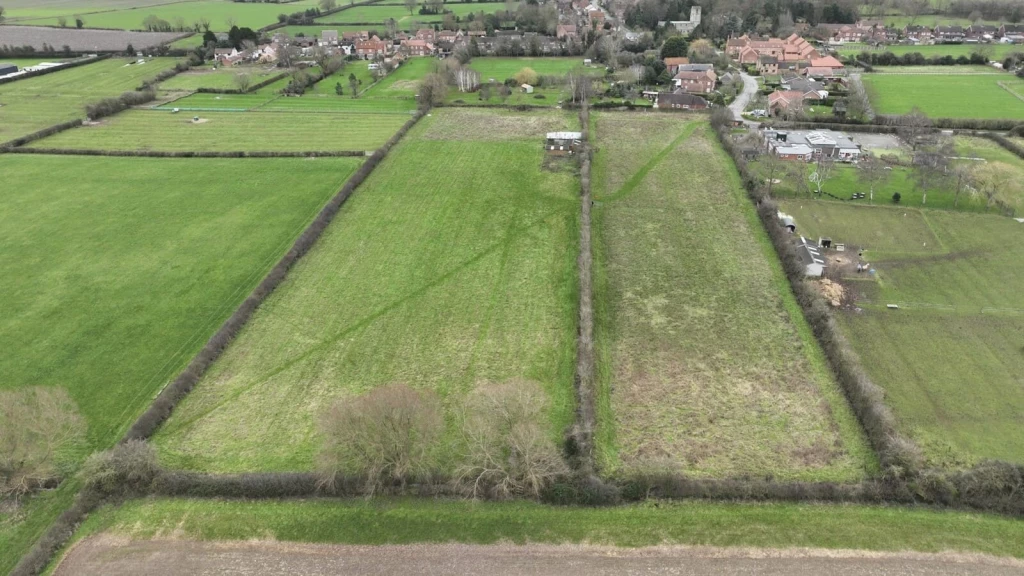 Aerial view of countryside fields near a village, showing divided small plots for sale in a typical land banking setup where micro-plots are marketed as “future development land” despite planning permission and access constraints.