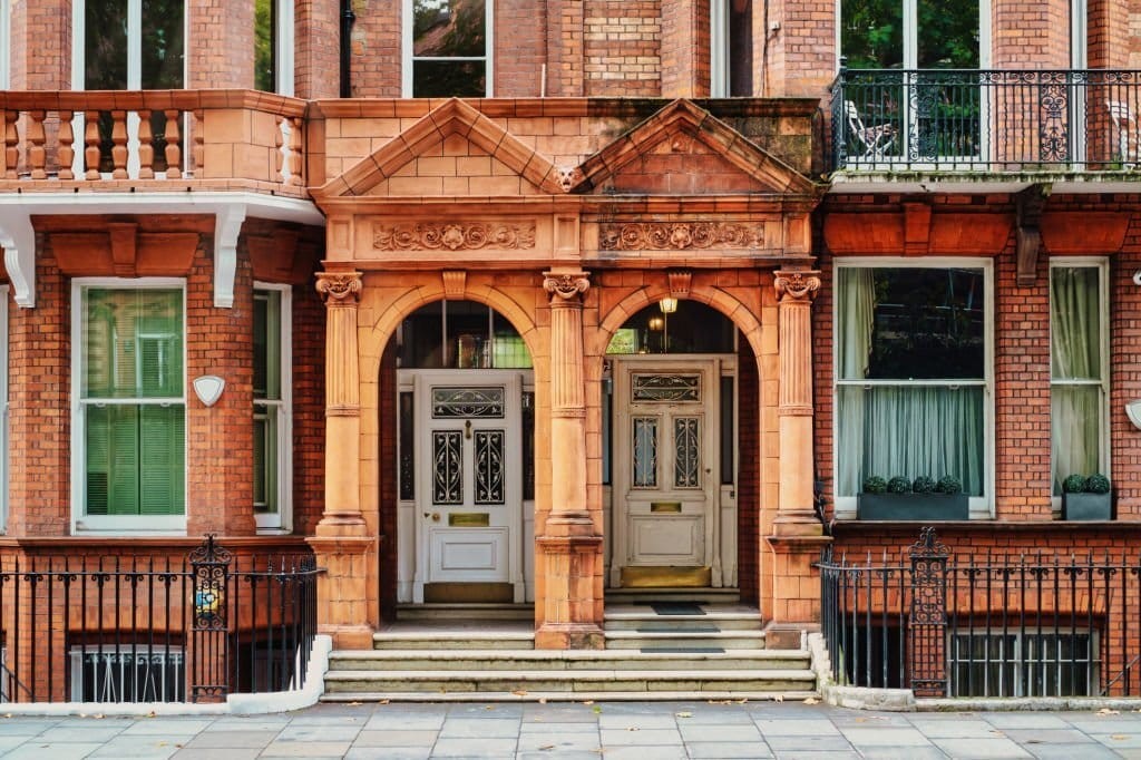 Street view of two beautiful red brick listed properties in central London with an arched access to the white front doors with gold door knobs, gold letter box and gold kick plate