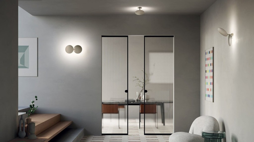 Minimalist interior design with neutral tones, featuring a plush seat, frosted glass doors, modern artwork, and sophisticated wall-mounted lights.